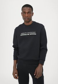Sort sweatshirt med rund hals, ribbede manchetter og kant. Fremhæver "ARMANI EXCHANGE 1991" logo i hvid og lyseblå på fronten.