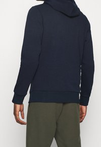 Tmavě modrá mikina s kapucí, klokankovým kapsou, přiléhavými manžetami a stahovací šňůrkou na kapuci; vyrobená z měkké a texturované látky.