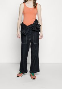 Orange Nike linne, oversized svarta denimjeans med vit sömnad, och flerfärgade sneakers med gröna, orange och svarta detaljer.