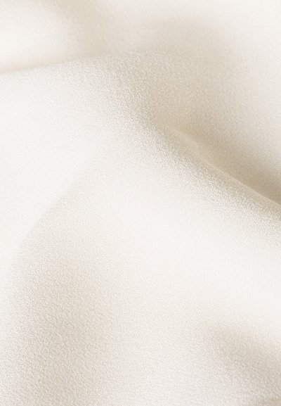 Tissu ivoire clair avec une surface lisse et légèrement texturée. Le matériau semble doux et fluide, avec un subtil éclat sous la lumière.