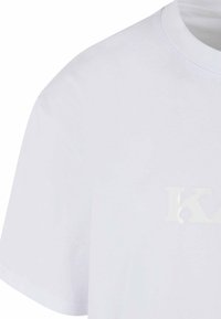 White cotton t-shirt featuring a crew neck, short sleeves, and a textured white logo detail on the front. Smooth texture, standard fit.
