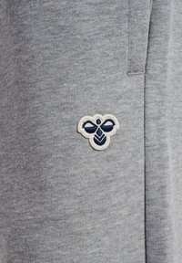 Szary materiał z małym granatowo-białym wyszywanym logo pszczoły w pobliżu pionowego szwu.