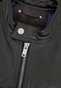 Schwarze Lederjacke mit hohem Kragen, silbernem Reißverschluss und Druckknopfdetails. Glatte Textur mit kontrastierendem Innenfutter.