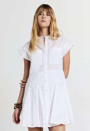 Weißes Baumwollkleid mit kurzen Ärmeln, Knopfverschluss, zwei Brusttaschen und gestickten Blumenmustern entlang des Rocks.