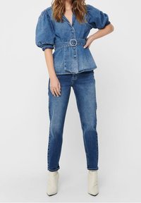 Denim blouse with puff sleeves and a cinched waist, featuring a large circular belt buckle, paired with fitted medium-blue jeans and off-white ankle boots.