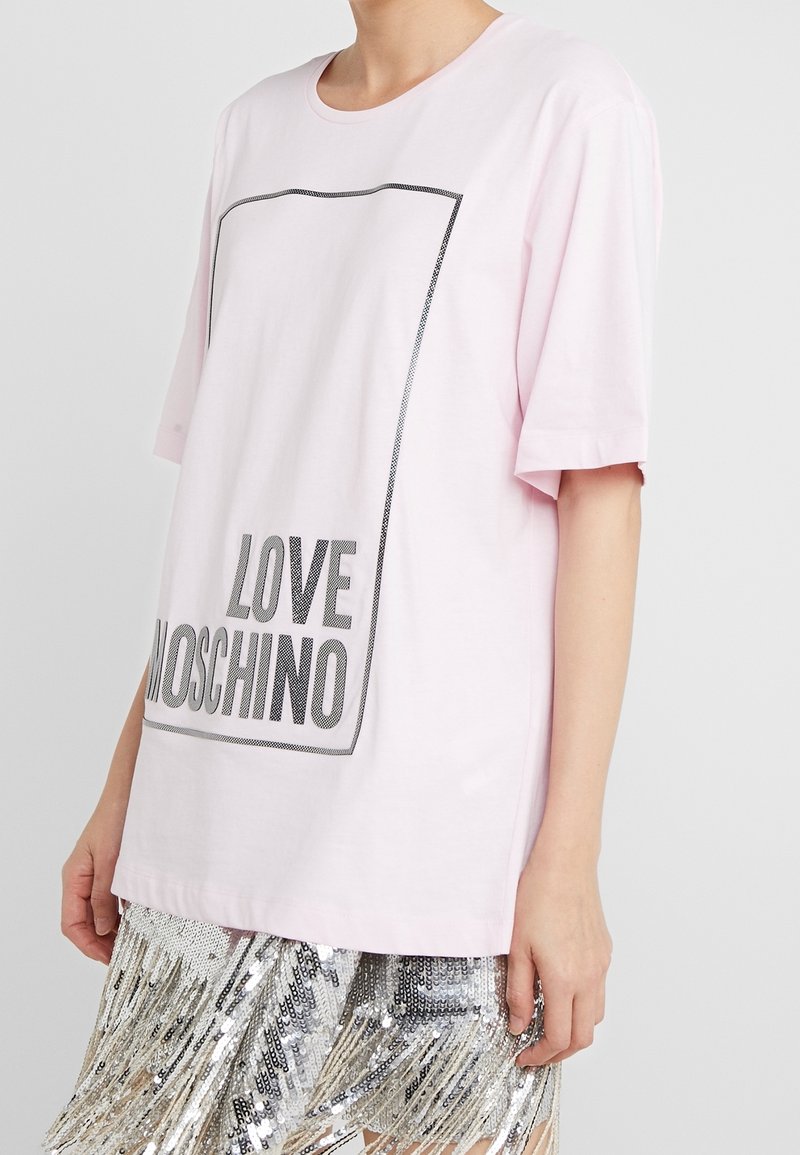 Růžové bavlněné tričko s krátkým rukávem, s černým obdélníkovým orámováním a textem "LOVE MOSCHINO" tučným šedým písmem ve spodní části.