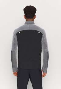 Zwarte lange mouwen jack met verticale zwart-witte gestreepte mouwen, hoge kraag en reflecterende accenten op de rug en schouders.