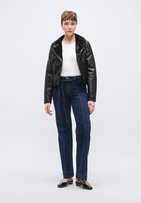 Μαύρο cropped δερμάτινο μπουφάν με γιακά από ψεύτικη γούνα, λευκό εφαρμοστό τοπ και ψηλόμεσο μπλε τζιν με διακοσμητικές ραφές. Μαύρα επίπεδα παπούτσια.