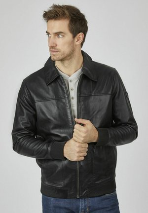 Black leather bomber jacket with a collar, front zipper closure, and ribbed cuffs. Worn over a light gray henley shirt.
