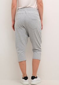 Grå bomulds cropped bukser med elastisk talje, der har baglommer og en afslappet pasform, parret med hvide sneakers med sorte detaljer.