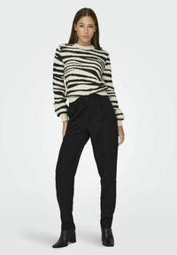 Black high-waisted trousers paired with a soft, cream sweater featuring black zebra stripes. The sweater has ribbed cuffs and neckline.