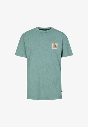 Morska bawełniana koszulka z nadrukiem z przodu, w połączeniu z czarnymi szortami jeansowymi i białymi tenisówkami, na jednolitym tle.