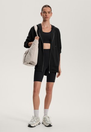 Musta vetoketjullinen huppari yhdistetty mustaan urheiluliiviin ja polviin ulottuviin pyöräilijänshortseihin. Vaaleanvärinen löysä laukku ja muhkeat lenkkarit. Yksinkertainen muotoilu.