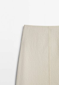 Ullkjol i krämfärgad med en texturerad yta; har en mittsöm och en figurnära design vid midjan.