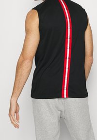 Black sleeveless top with a red and white stripe down the back. Features logo accents within the stripe. Material appears lightweight.