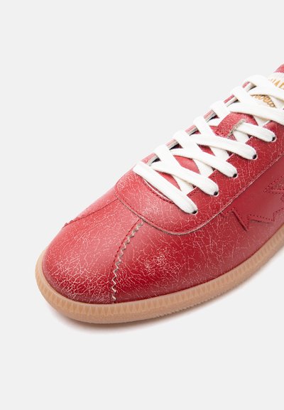 Baskets en cuir rouge avec lacets blancs, semelle en caoutchouc, et détail latéral en forme d'étoile montrant une finition texturée et craquelée.