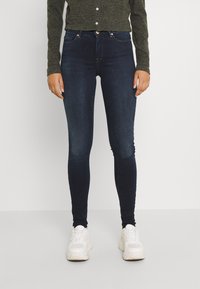 Ši slim-fit tumesinised denim püksid, millel on keskmine talje ja õrn fade, on kokku sobitatud valgete sneaker'itega.