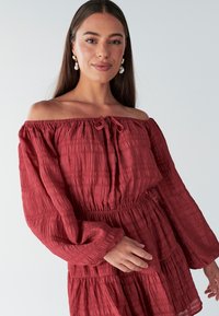 Rode blouse met off-shoulder, textuur, pofmouwen en een getailleerde tailleband. Heeft een trekkoordje bij de halslijn en een gelaagd ontwerp.