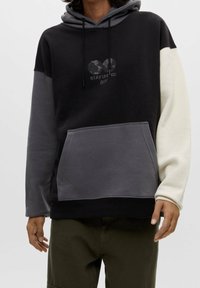 Sudadera con capucha en negro, gris y crema, que presenta un bolsillo frontal, cordones y un diseño gráfico "STAY UNITED" en el pecho.