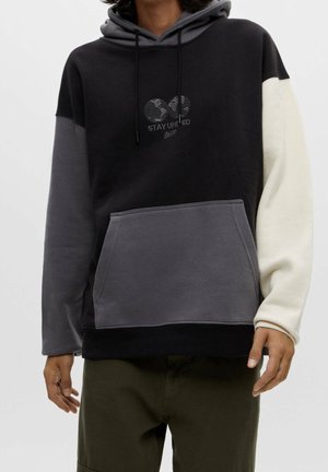 Sweat-shirt à capuche en noir, gris et crème, comportant une poche frontale, des cordons de serrage et un design graphique "STAY UNITED" sur la poitrine.