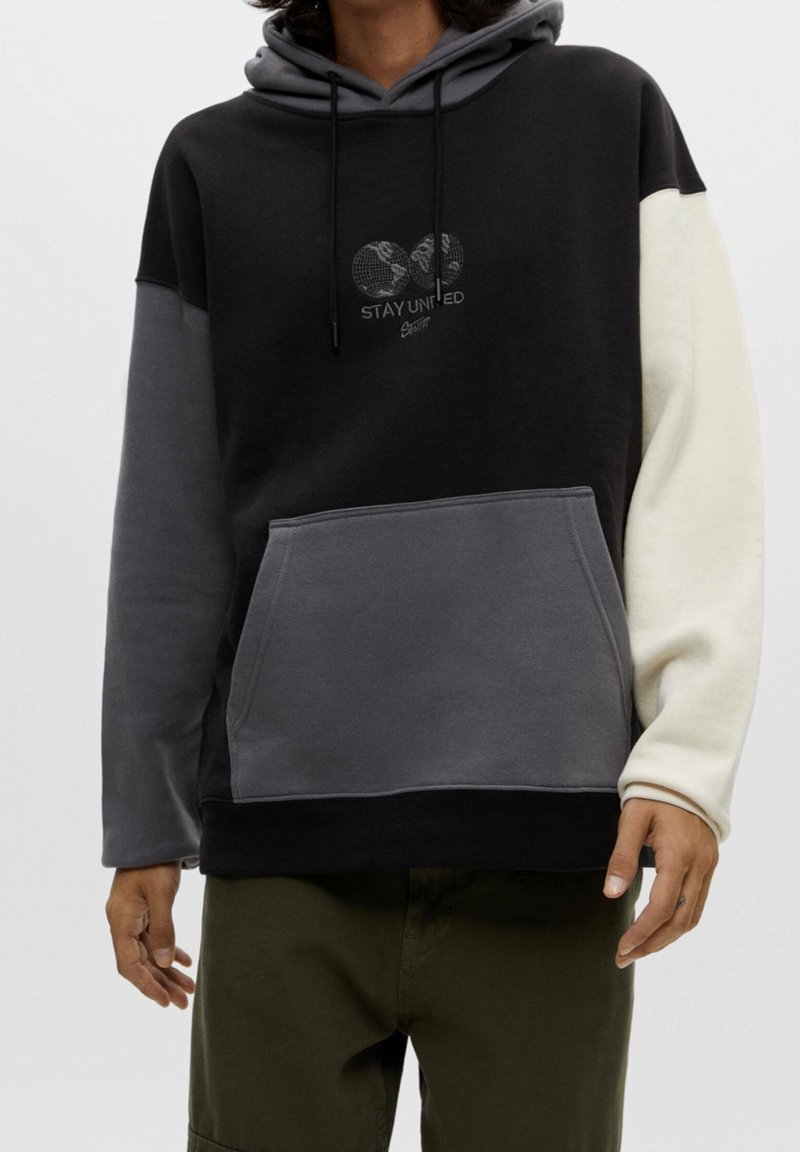 Sudadera con capucha en negro, gris y crema, que presenta un bolsillo frontal, cordones y un diseño gráfico "STAY UNITED" en el pecho.