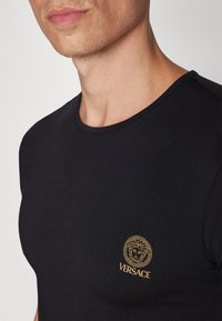 Crna pamučna majica s okruglim izrezom, kratkim rukavima i zlatnim Versace logom s emblemom Meduze na prsima.