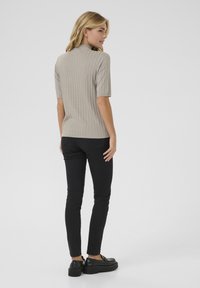 Beige ribbad t-skjorte med høy krage og korte ermer, sammen med slim-fit svarte jeans og svarte plattformsko. Glatt tekstur, tettsittende design.