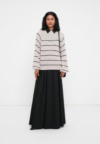 Hellgrauer, gestreifter Pullover aus weichem Material, kombiniert mit einem lockeren, schwarzen Maxirock. Der Pullover hat einen runden Kragen und überschnittene Schultern.