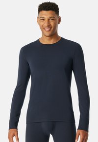 Maglietta navy a manica lunga in un tessuto morbido, caratterizzata da un collo rotondo, design aderente e maniche lunghe, ideale per essere indossata a strati.