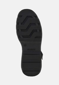 Suola di scarpa in gomma nera con motivo a zigzag testurizzato, logo del marchio in rilievo e bordi scanalati per trazione e aderenza.