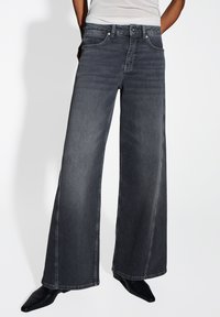 Donkergrijze wijde denim jeans met een gladde textuur. Beschikt over vijf zakken en gestikte details langs de naden.