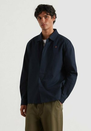 Camicetta blu navy con bottoni, dalla vestibilità comoda, colletto piatto e piccolo logo decorativo. Realizzata in tessuto morbido, con maniche lunghe e orlo dritto.