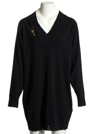 Czarny, oversize sweter z dekoltem w serek i długimi rękawami na białym manekinie, z dwoma złotymi broszkami w formie agrafek na lewym ramieniu.