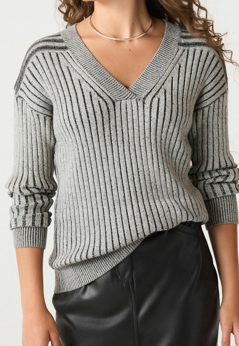 Pull gris côtelé avec un col en V, présentant des rayures noires et un tissu texturé. Manches longues avec un léger tombé et une taille ajustée.