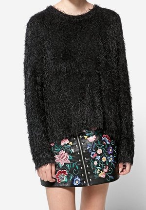 Pull noir duveteux à manches longues associé à une mini-jupe en cuir noire ornée de broderies florales colorées et d'une fermeture éclair à l'avant.