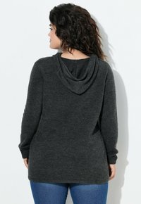 Sweat à capuche oversize gris foncé avec une texture douce, manches longues et col bénitier. Porté avec un jean denim bleu. Design simple.