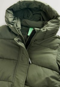 Olivenfarvet puffer vest med hætte, med lynlås foran, knaplukninger og quiltet tekstur. Inkluderer et brandmærke.