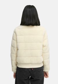 Crème pufferjack met een gestructureerde, fluffy buitenkant. Bevat horizontaal gestikte patronen en ribgebreide manchetten en zoom voor een snug fit.
