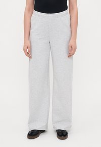 Ανοιχτό γκρι φαρδιά παντελόνια φόρμας από μαλακό ύφασμα, με ελαστική μέση και πλαϊνές τσέπες, συνδυασμένα με μαύρα υποδήματα.