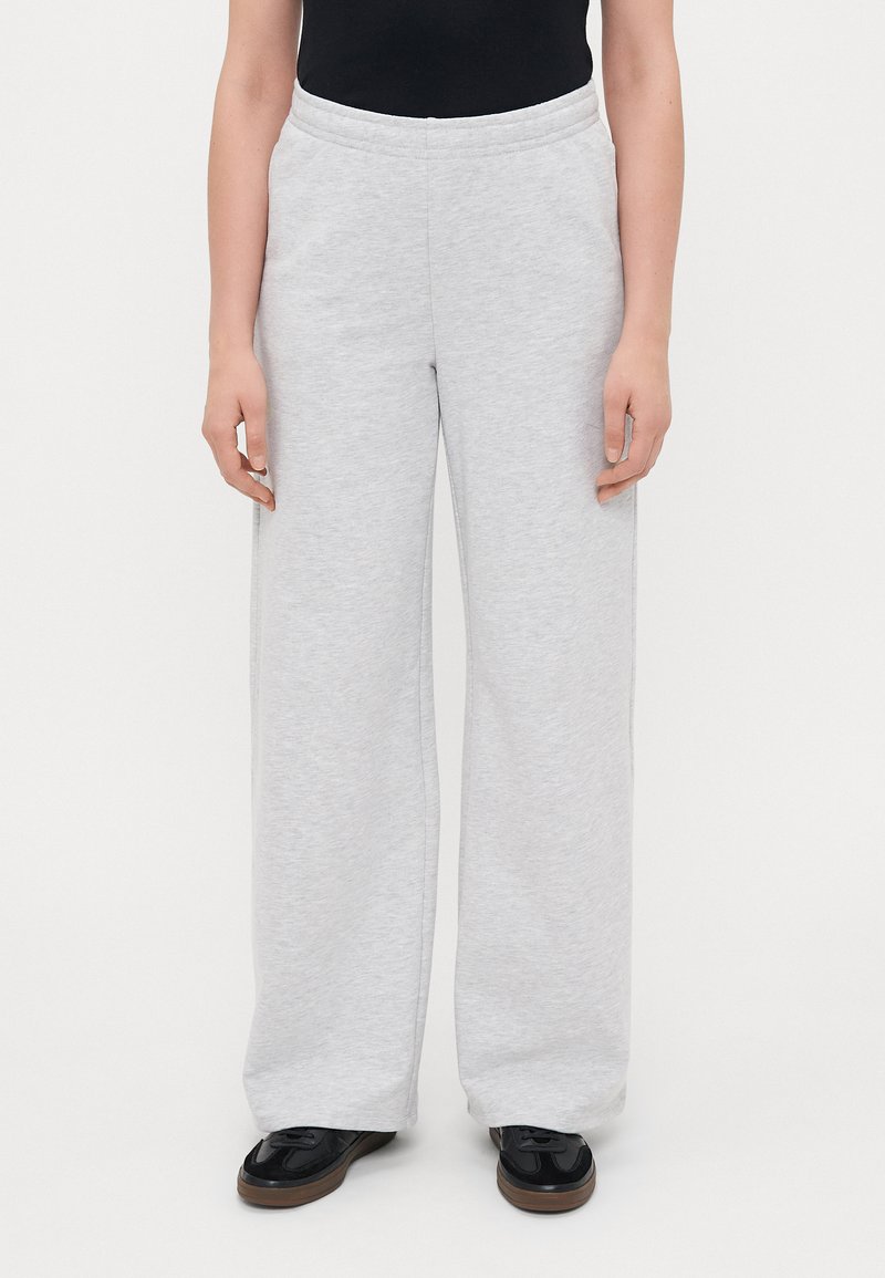 Ανοιχτό γκρι φαρδιά παντελόνια φόρμας από μαλακό ύφασμα, με ελαστική μέση και πλαϊνές τσέπες, συνδυασμένα με μαύρα υποδήματα.