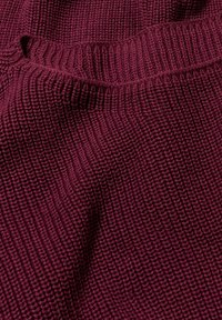 Tejido de punto burdeos con un patrón de relieve texturizado, que presenta un escote amplio y una caída relajada. Material suave y elástico.