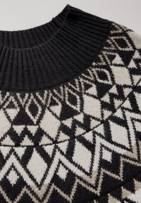 Schwarzer und crèmefarbener Strickpullover mit einem gerippten Kragen und geometrischen Mustern aus Rauten und Dreiecken in kontrastierenden Farben.
