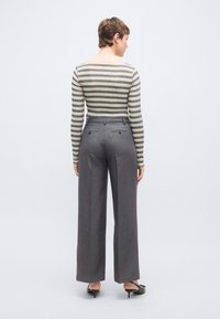 Μπλούζα με ρίγες και μακριά μανίκια σε μπεζ και πράσινο, συνδυασμένη με ψηλόμεσο, γκρι παντελόνι φαρδιάς γραμμής. Διαθέτει διπλές πίσω τσέπες και επίπεδη μπροστινή όψη.