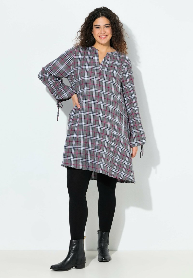 Abito tunica a quadri in grigio, rosa e bianco; presenta maniche lunghe con lacci, scollatura a V e una vestibilità comoda. Indossato con leggings neri e stivaletti.