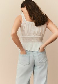 Top blanc sans manches avec taille froncée et ourlet en peplum porté avec un jean taille haute bleu clair. Motif de petits pois subtil sur le tissu.