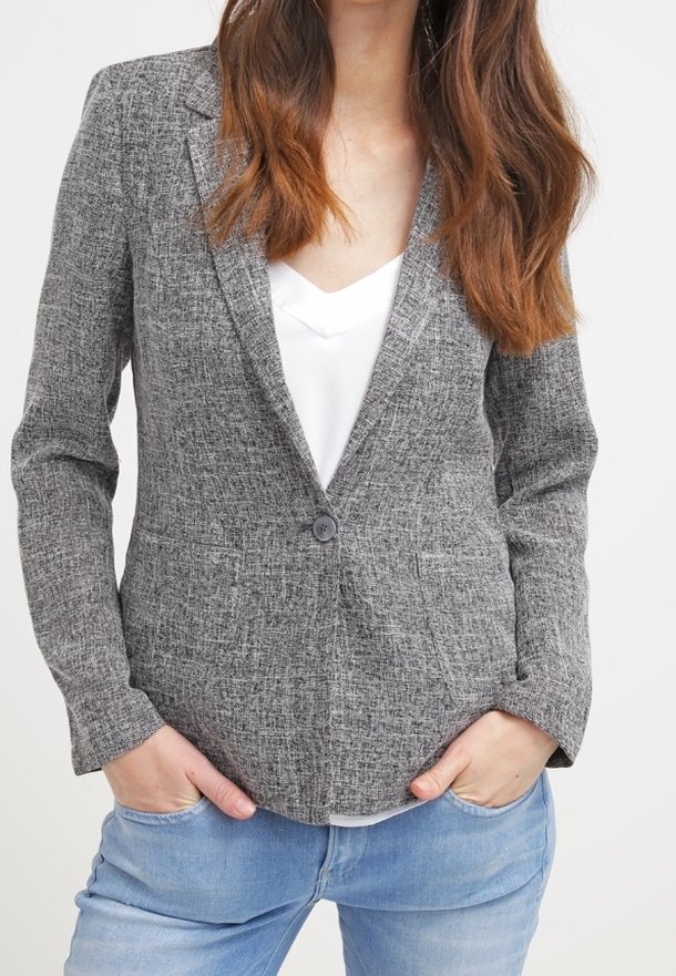 Blazer gris texturé avec col à revers cranté, fermeture à un bouton et deux poches avant. Porté sur un haut blanc, associé à un jean clair.