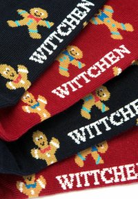 Cuatro calcetines estampados con diseños de muñecos de jengibre en marrón, azul y rojo sobre fondos negros y rojos con el texto "WITTCHEN".