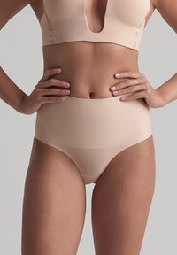 Slip beige a vita alta realizzato in tessuto morbido, con un design senza cuciture e una fascia larga per comfort e copertura.