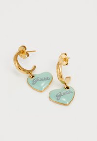 Pendientes de aro dorados con charms en forma de corazón de color verde menta que presentan la palabra "Guess" en gris. Acabado suave y brillante con detalles en relieve.
