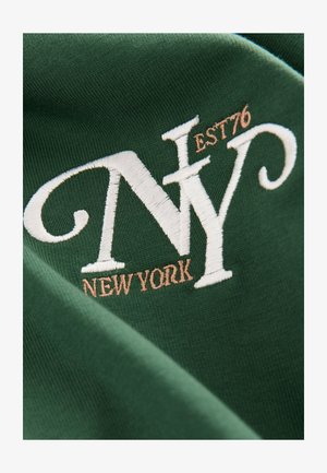 Zielona tkanina z białą i brązową haftem z napisem "NY" oraz "NEW YORK EST 76", charakteryzująca się gładką fakturą i klasycznym wzorem.